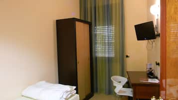 A hotel room with a bed, a desk, a chair, a wardrobe, a television, and a window with blinds.