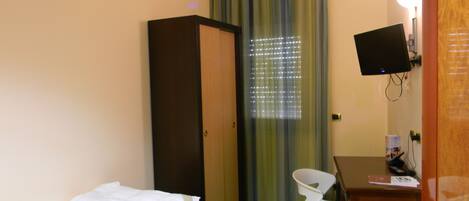 A hotel room with a bed, a desk, a chair, a wardrobe, a television, and a window with blinds.
