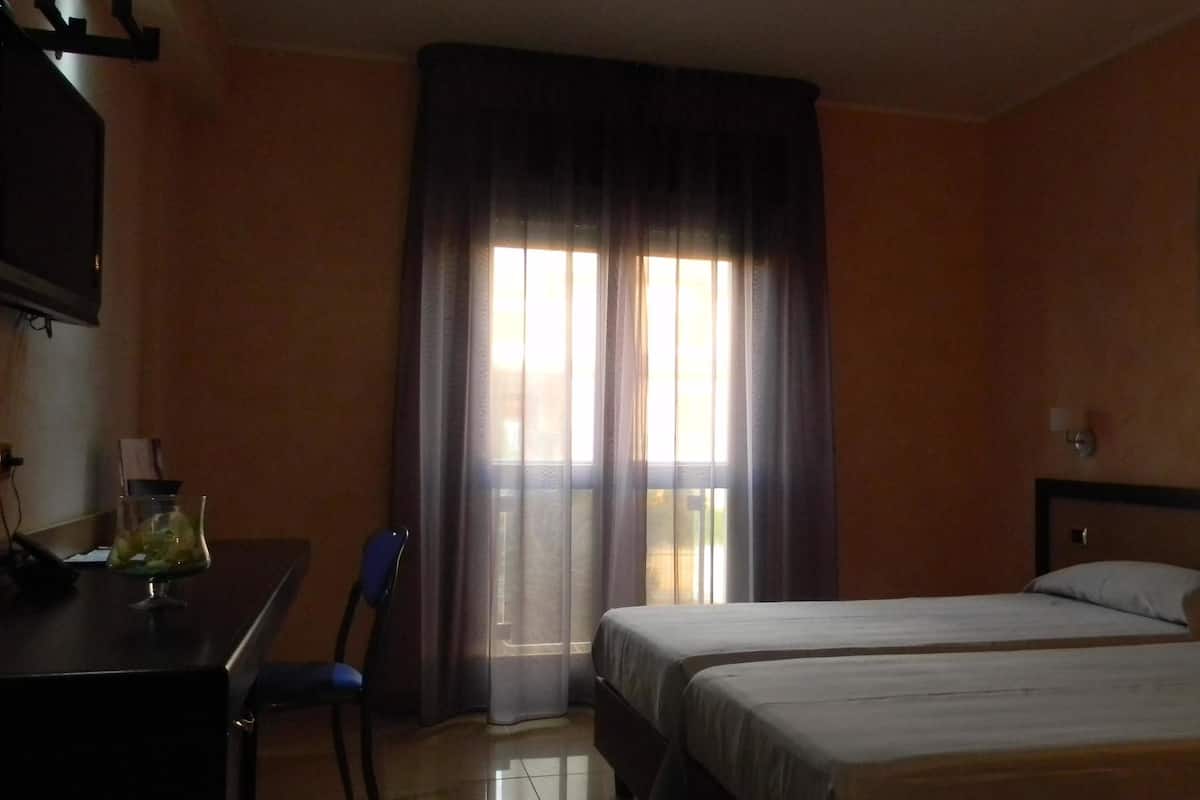 A hotel room with two beds, a desk, a chair, and a window with curtains.