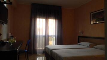 Une chambre d’hôtel avec deux lits, un bureau, une chaise et une fenêtre avec des rideaux.