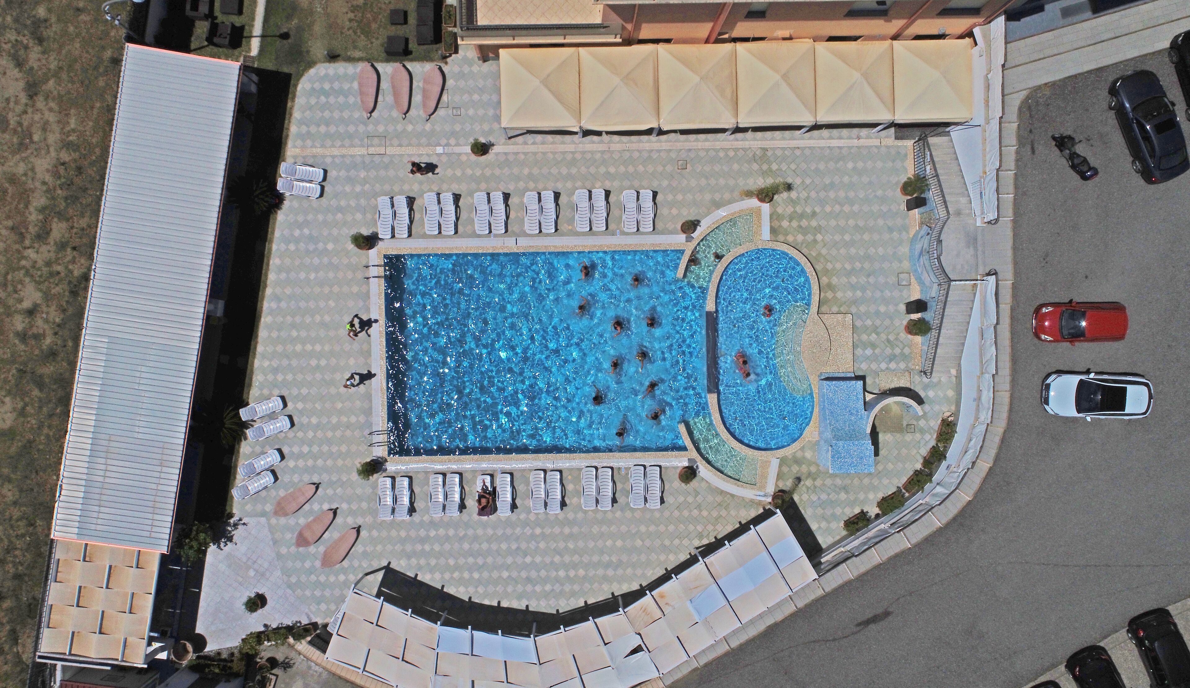 Vista aérea de una zona de piscina con sillones de descanso y sombrillas.