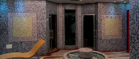 Uma área de spa com paredes em mosaico, um elemento de água circular e uma cadeira de lounge.