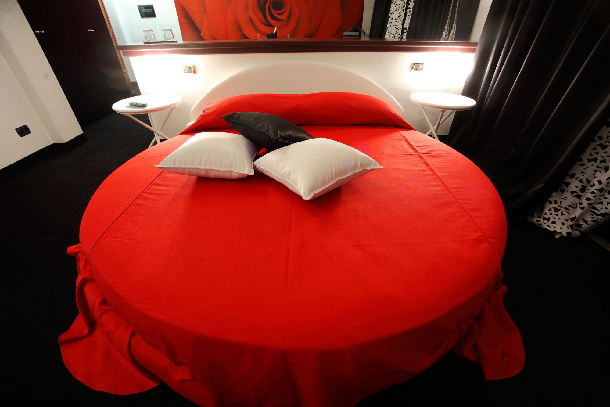 A bed with a red bedspread, two white pillows, and a black pillow. There are two bedside tables with lamps.