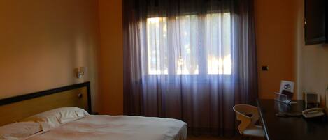 A hotel room with a bed, a desk, a chair, and a TV.