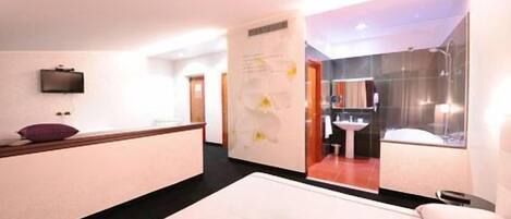 A hotel room with a bed, a desk, a mirror, and a bathroom visible through an open door.