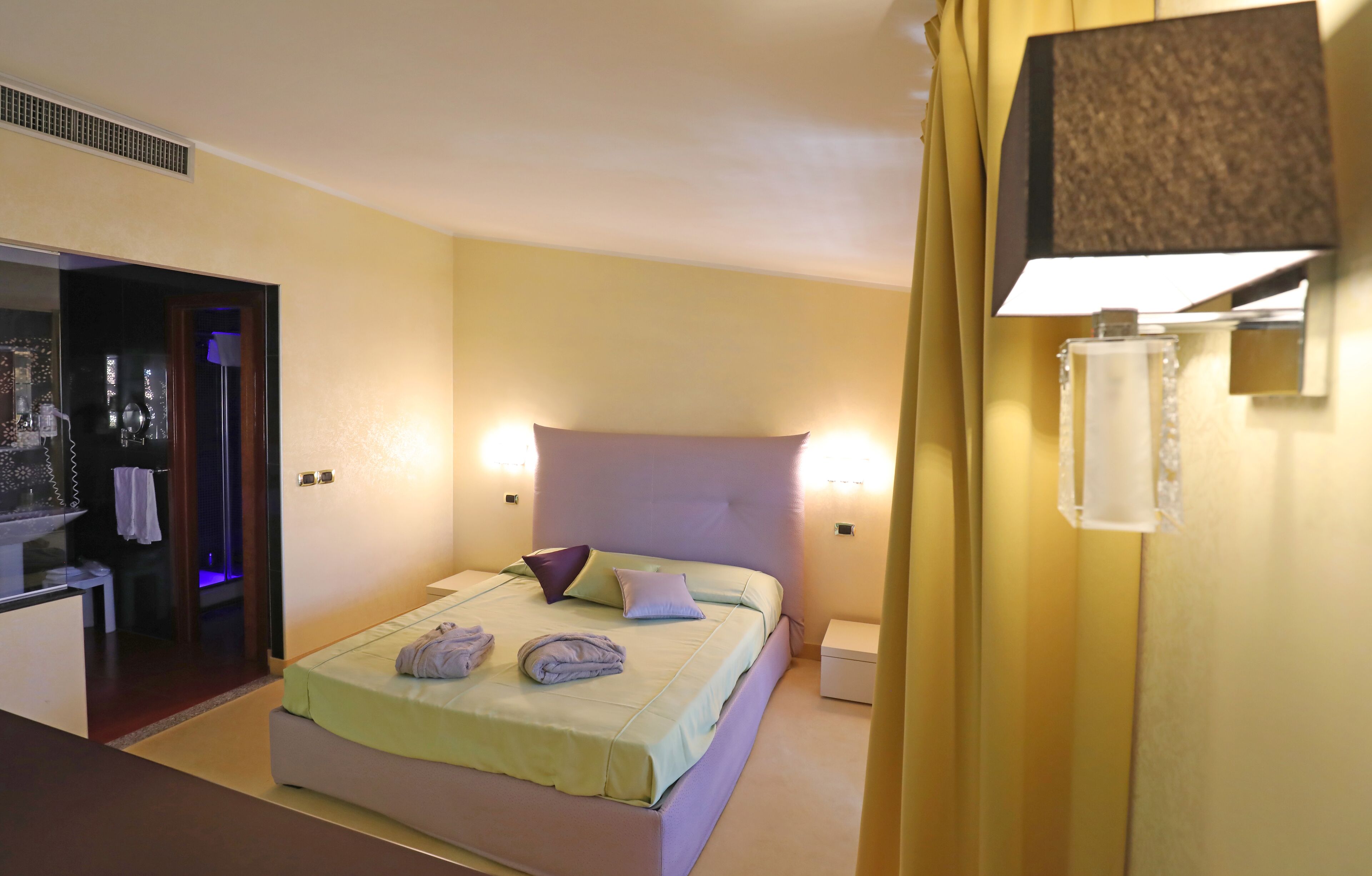 A hotel room with a bed, bedside lamps, a nightstand, and a bathroom visible through an open door.