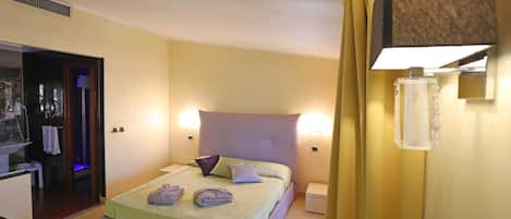 A hotel room with a bed, bedside lamps, a nightstand, and a bathroom visible through an open door.