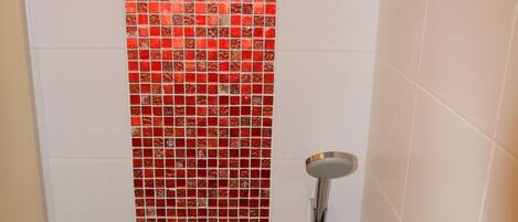 A shower with a red mosaic tile design on the wall, a chrome showerhead, and a handheld showerhead.