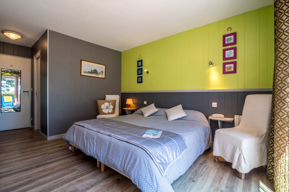 A bedroom with a large bed, a chair, a nightstand, and a wall with framed pictures.