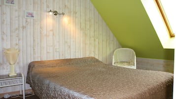 A bedroom with a wooden wall, a bed with a patterned bedspread, a small table with a lamp, and a chair.