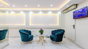 Una habitación moderna con sillas color turquesa, una mesita redonda y un televisor en la pared.