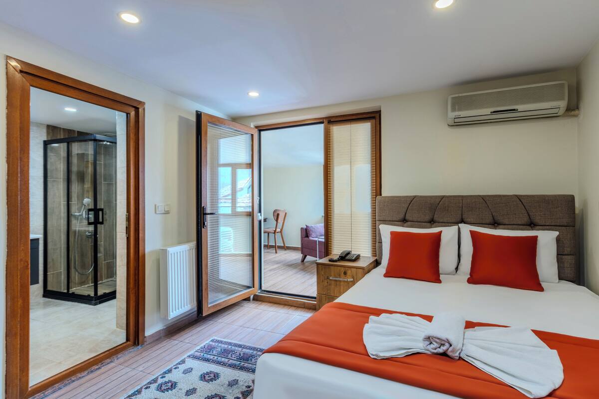 A hotel room with a large bed, a shower, a sliding glass door to a balcony, and a ceiling-mounted air conditioner.