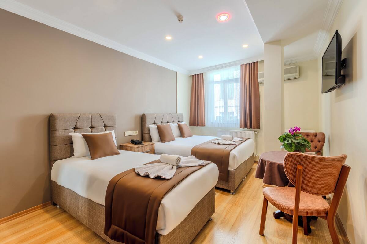 A hotel room with two beds, a chair, a table, and a TV.
