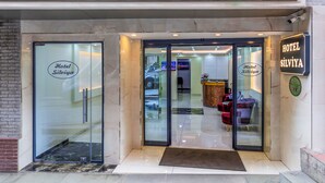 La entrada del Hotel Silviya, con un puerta de vidrio, un mostrador de recepción y un área de estar visible en el interior.