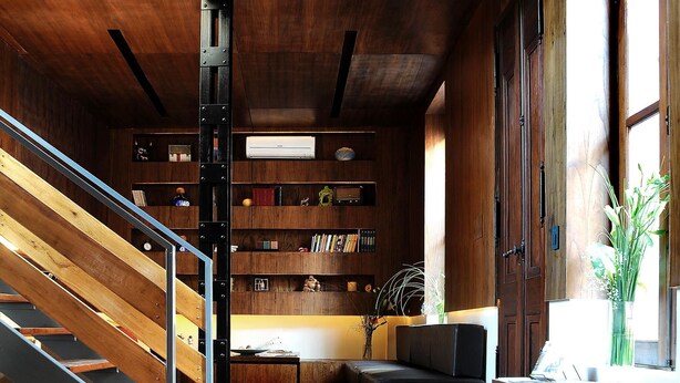 Een modern interieur met een houten trap, een zwarte bank, een bijzettafeltje en een boekenkast.
