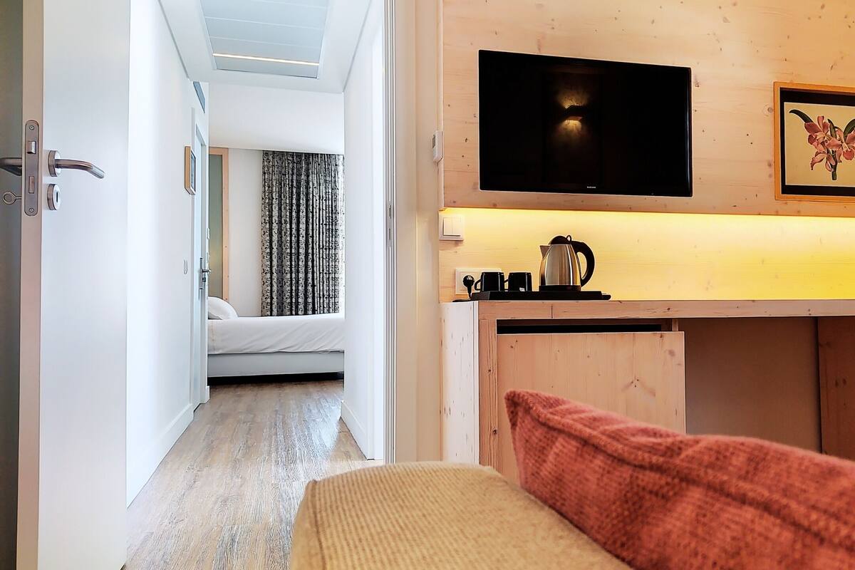 Une petite chambre comprenant un lit, un coin cuisine, une télévision et un tableau encadré accroché au mur.