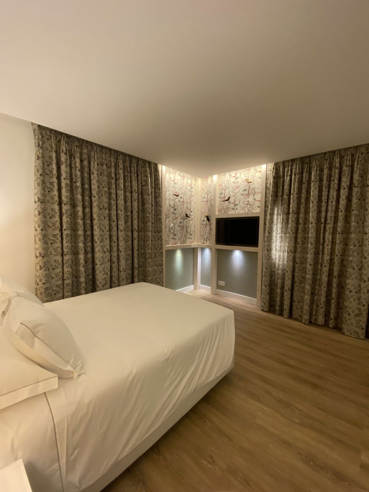 A bedroom with a bed, curtains, a TV, and a small window.