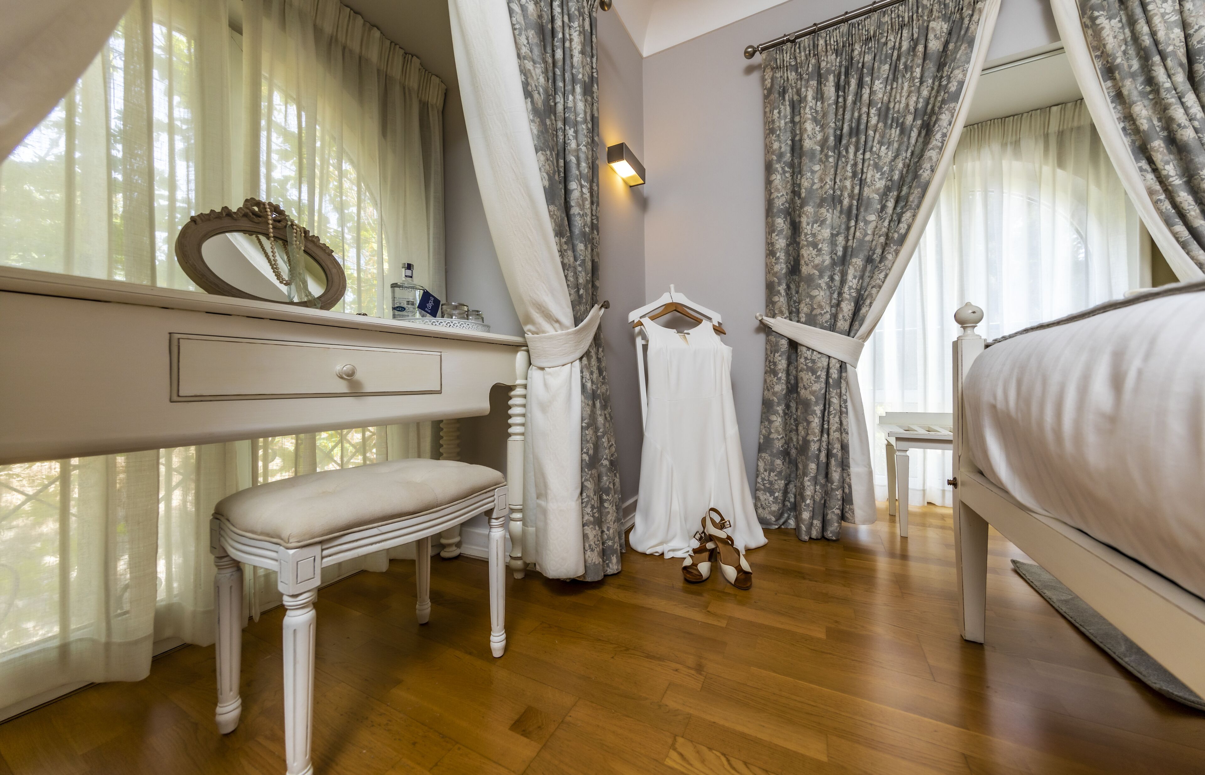 Een slaapkamer met een houten vloer, een wit bed, een nachtkastje, een spiegel en een hangende badjas.