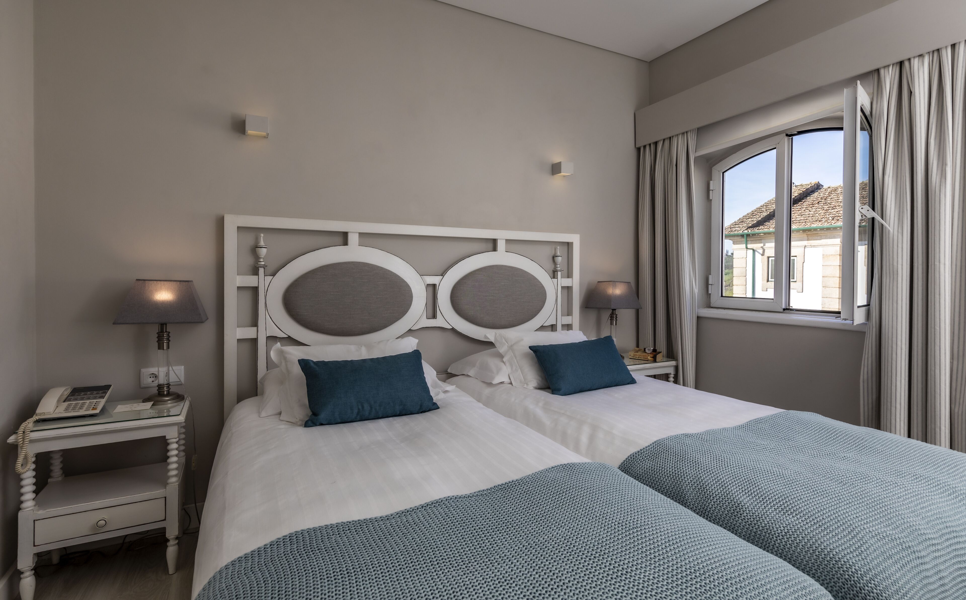 Habitación de hotel con cama doble, dos mesitas de noche, lámpara, teléfono y ventana con cortinas.