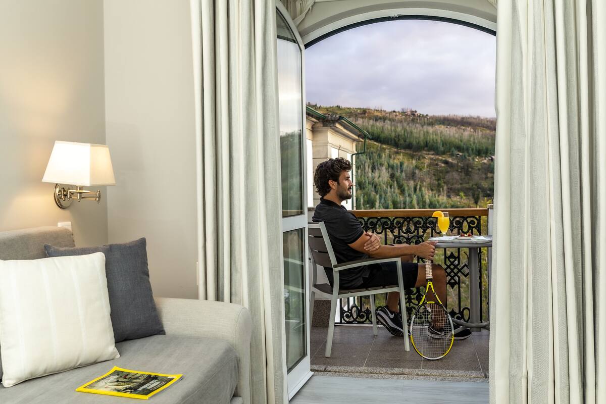 Une chambre d’hôtel avec un balcon, un canapé, une table et une raquette de tennis.