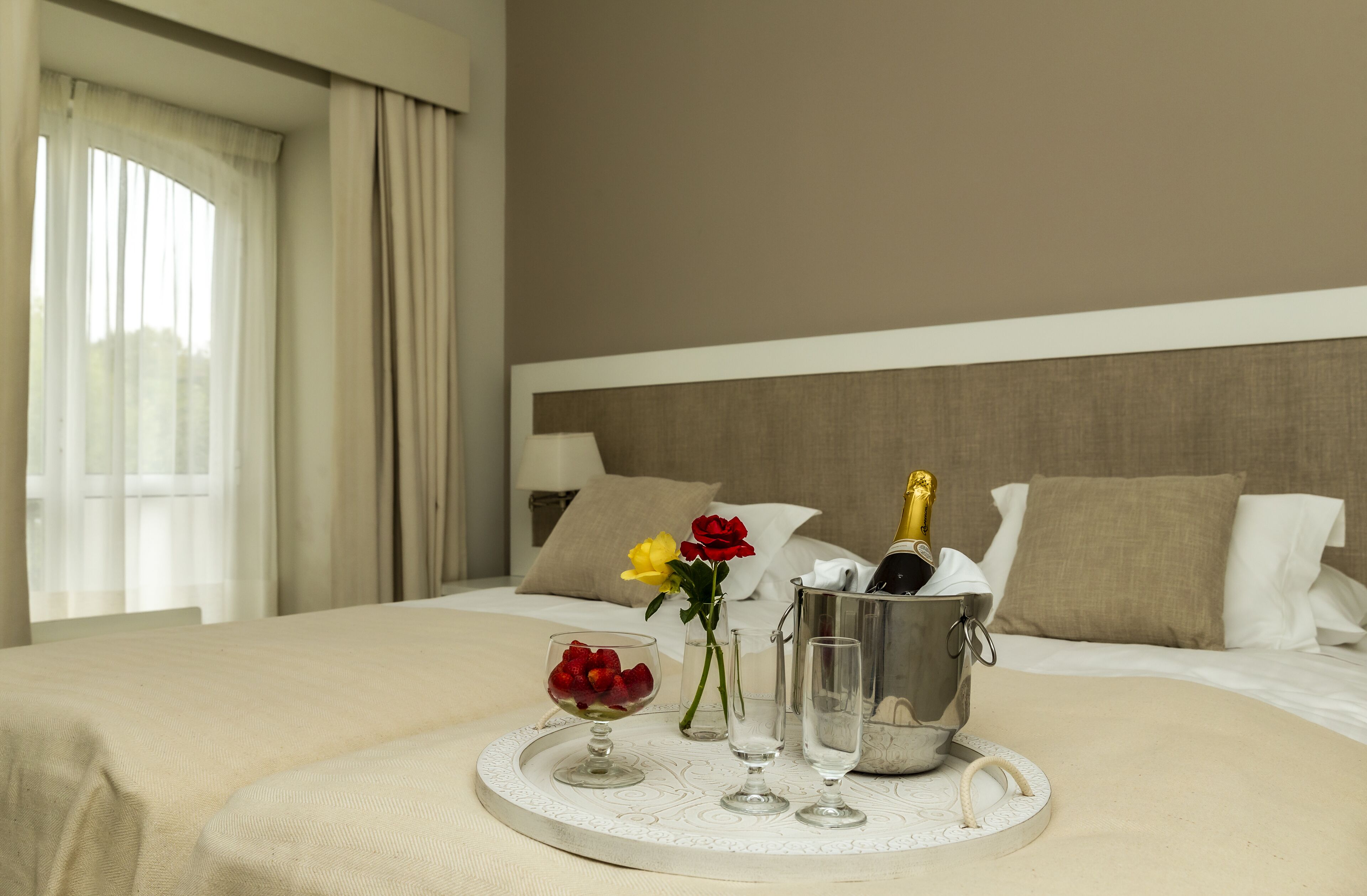 Ein Hotelzimmer mit einem ordentlich bezogenen Bett, einem Nachttisch mit Champagner, Gläsern und Blumen.
