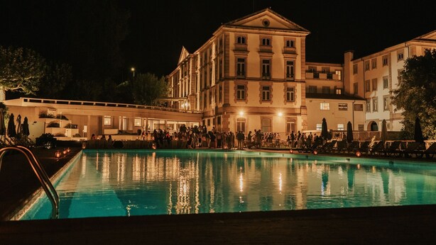 A large, illuminated swimming pool with a crowd of people around it, surrounded by historic buildings with classical architecture. - Grande Hotel das Caldas da Felgueira (Nelas)