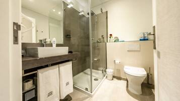 Un baño moderno con ducha de vidrio, lavamanos blanco y retrete.