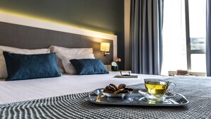 A neatly made bed with pillows, a tray with a cup of tea and some snacks, and a nightstand with a lamp and a clock. - Grande Hotel das Caldas da Felgueira (Nelas)