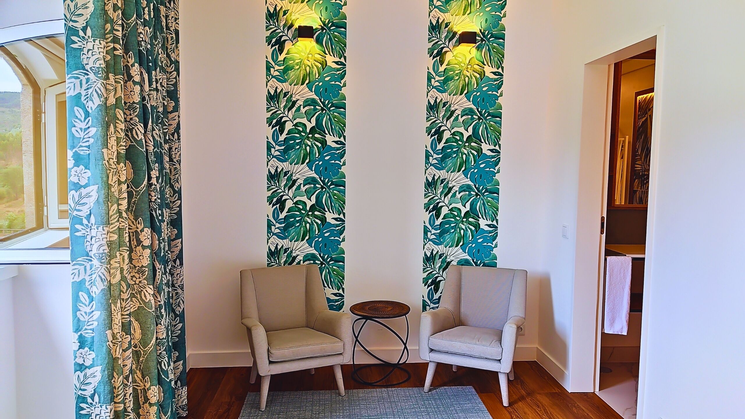 A room with two armchairs, a small round table, and curtains with a tropical leaf pattern.