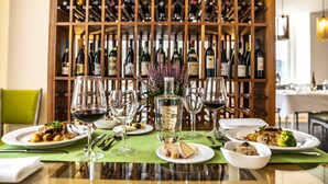 A dining table set with plates of food, wine glasses, and a bottle of Grand Cru wine. In the background, there is a wooden wine rack filled with various bottles. - Grande Hotel das Caldas da Felgueira (Nelas)