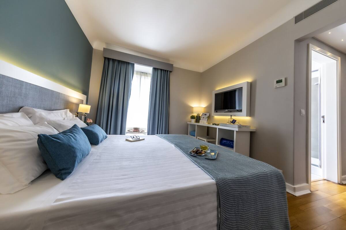 Une chambre d’hôtel avec un grand lit, un bureau avec une télévision et une fenêtre avec des rideaux.