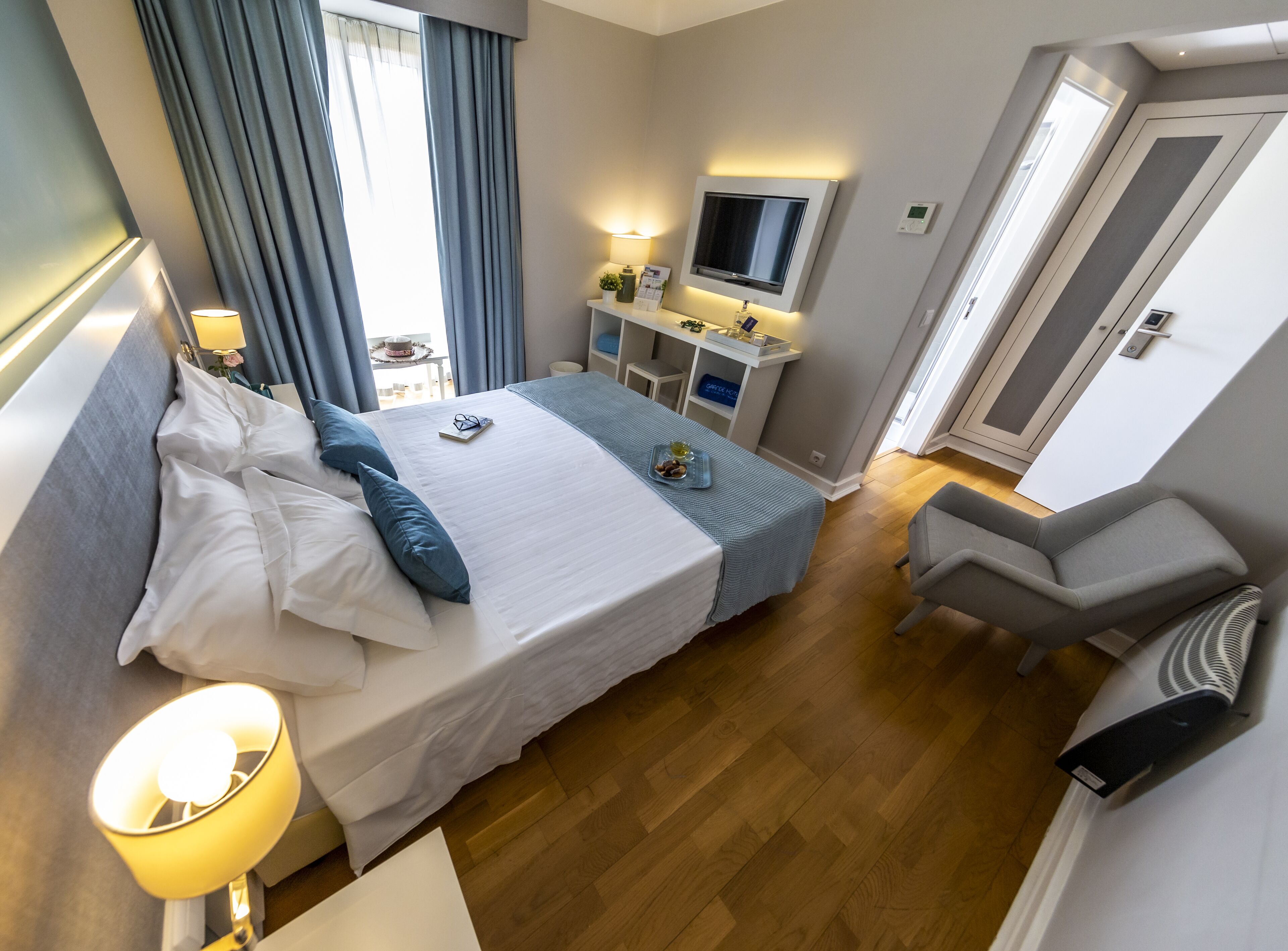 A hotel room with a bed, bedside table, lamp, TV, desk, chair, and a wardrobe.