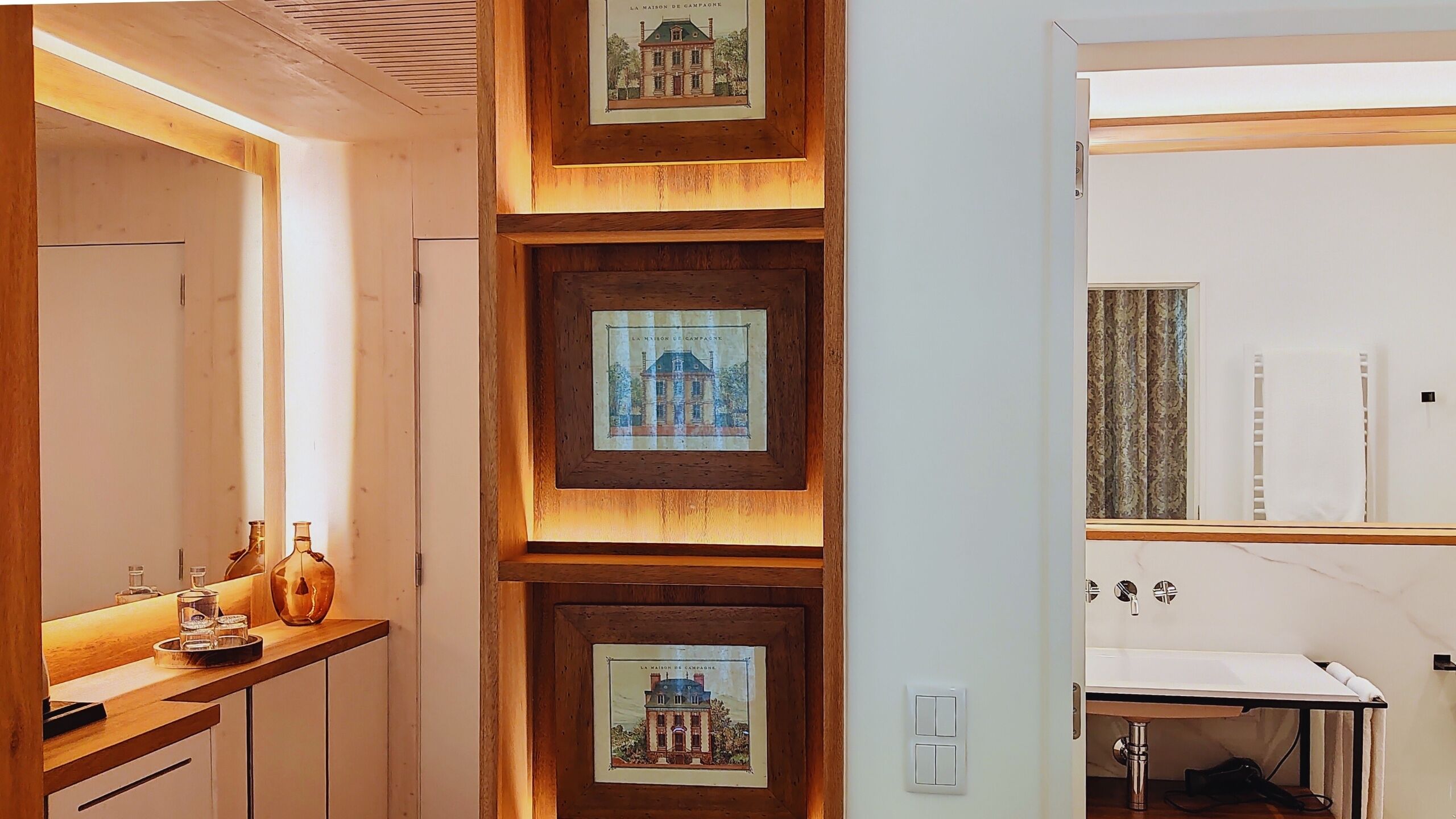 A modern bathroom with a wooden vanity, a mirror, and framed pictures on the wall.