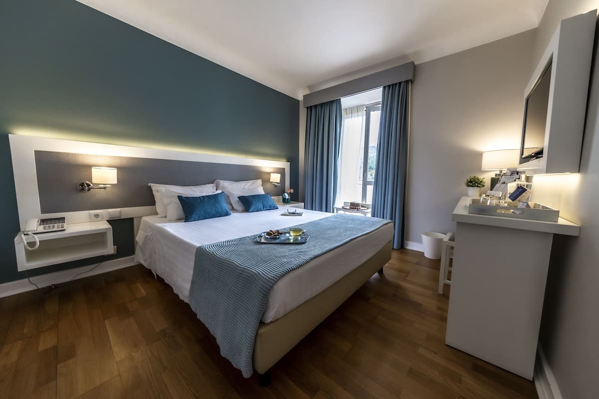Une chambre d’hôtel moderne avec un grand lit, des tables de chevet, un bureau et une fenêtre avec des rideaux.