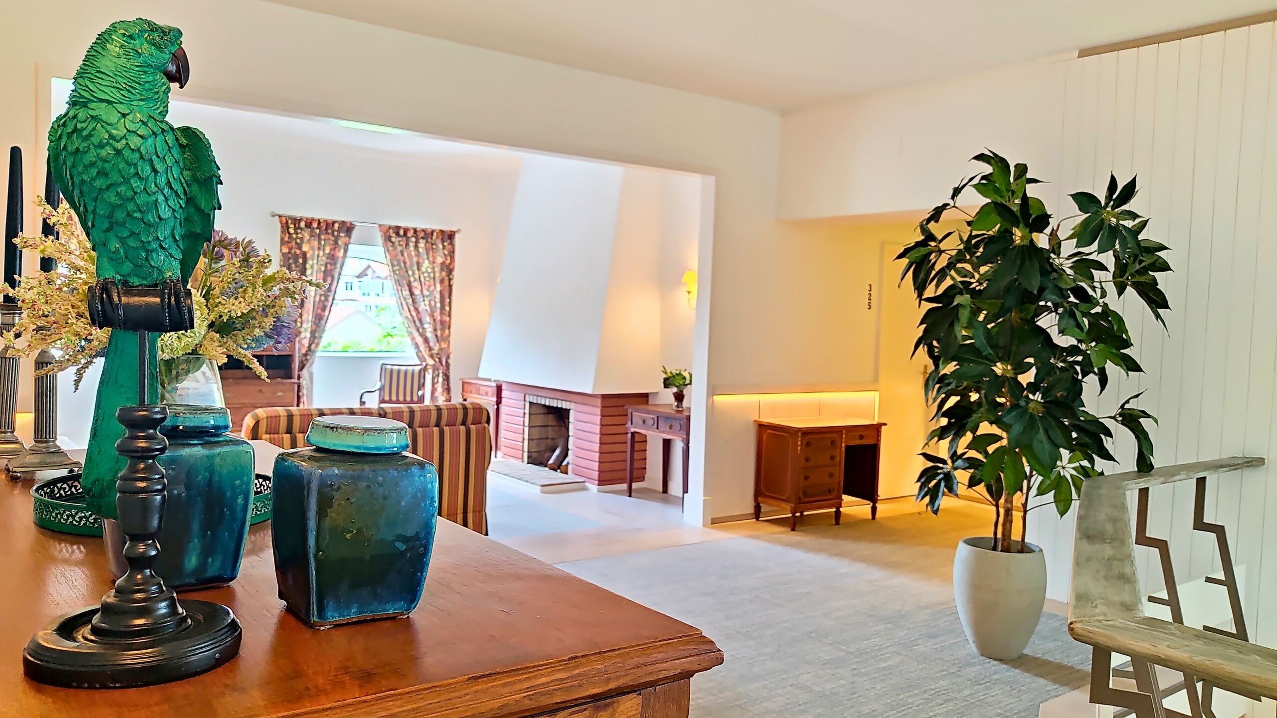 A spacious living room with a wooden coffee table, a green parrot sculpture, and a large potted plant.