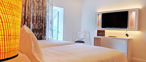 Una habitación de hotel con dos camas, un televisor montado en un mueble blanco, una silla y una ventana con cortinas.