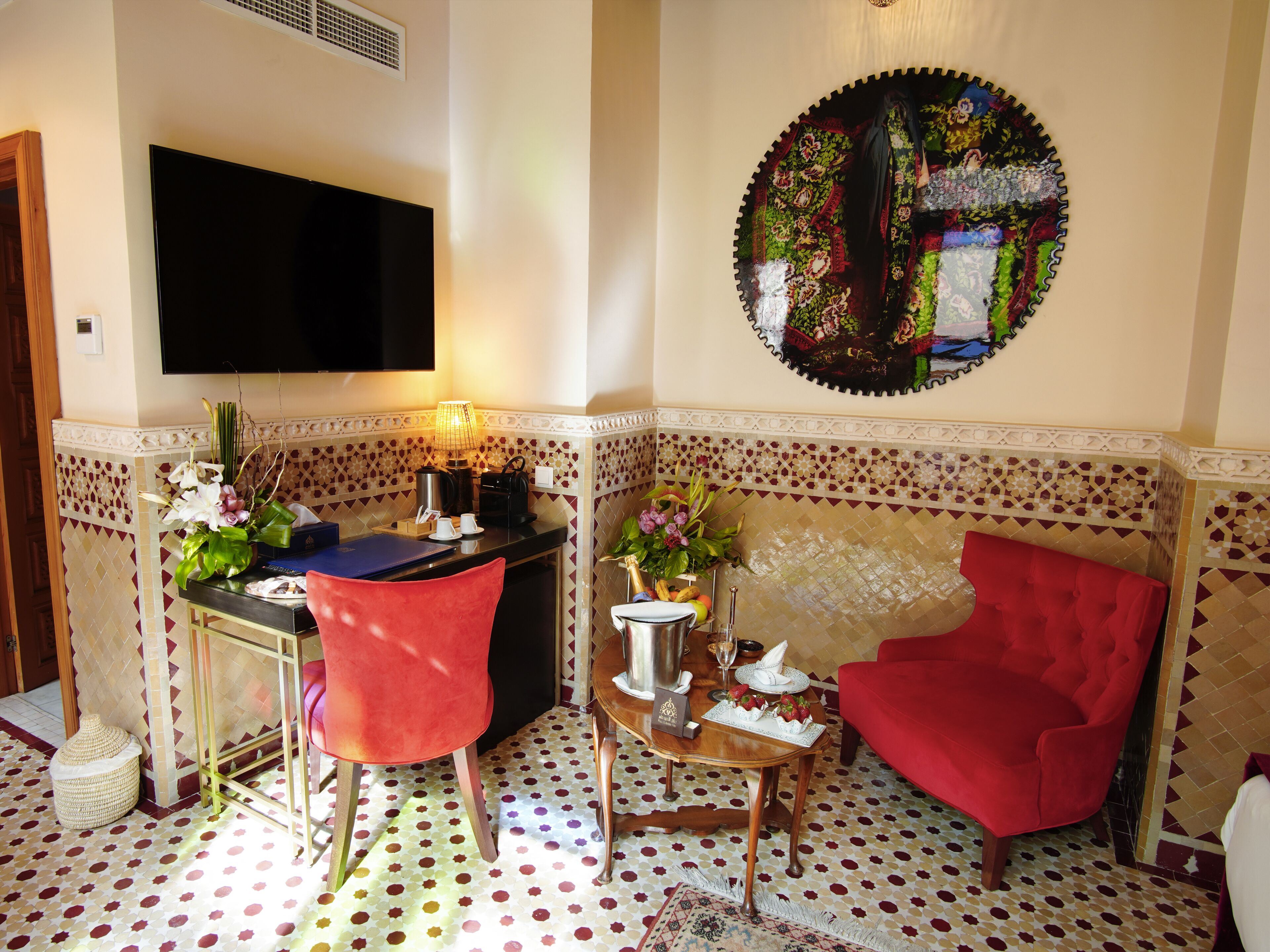 A room with a dining table, chairs, a sofa, a TV, and a decorative wall piece.