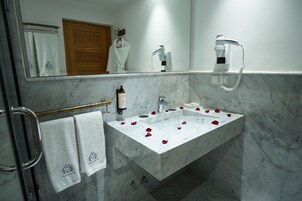 Casa de banho com lavatório de mármore, suporte de toalhas com duas toalhas, secador de cabelo e frasco de champô.