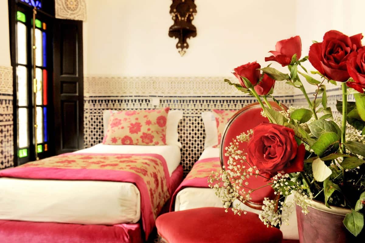 Una habitación con dos camas, un jarrón con rosas rojas y un papel tapiz estampado.