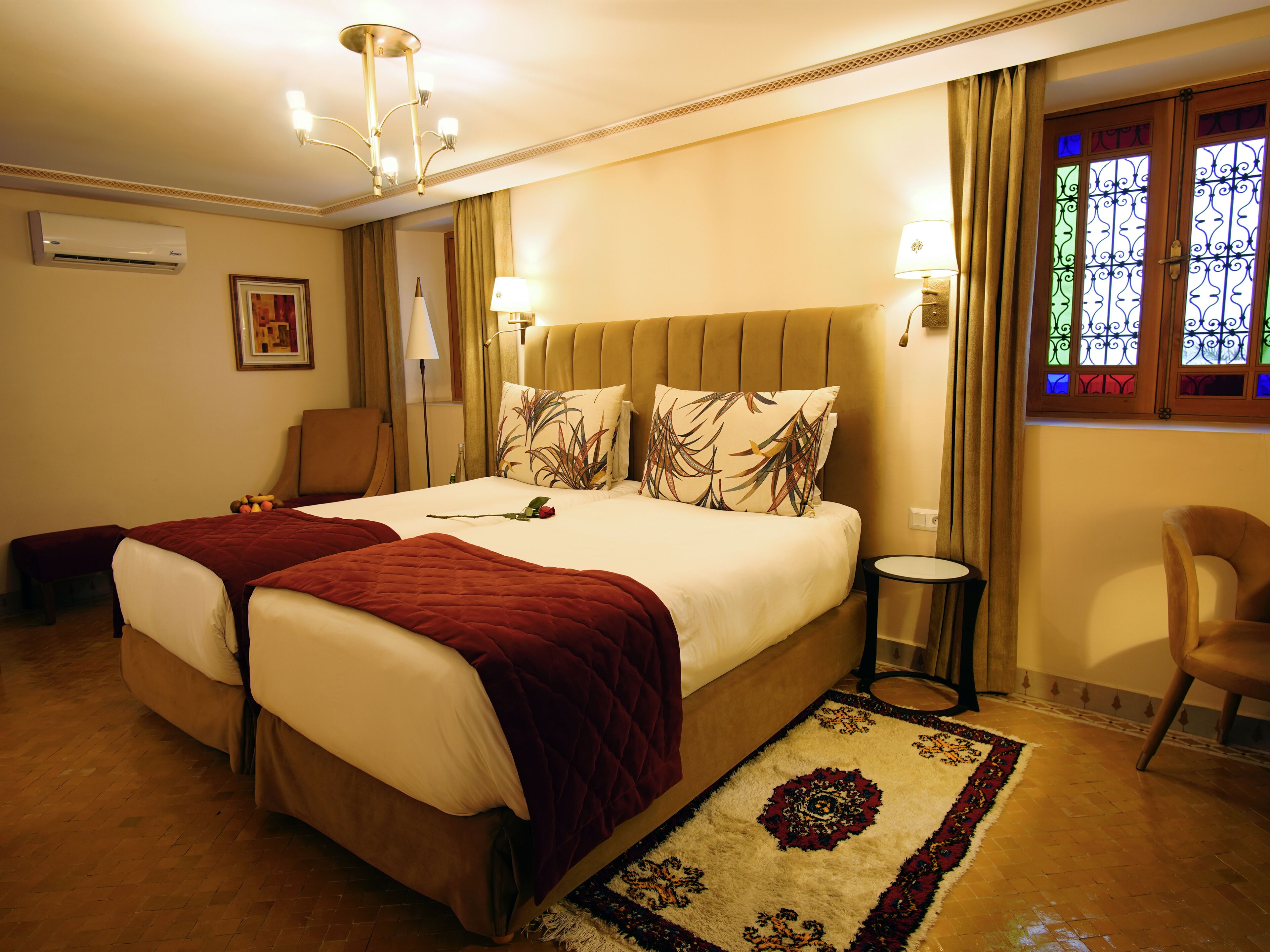 A hotel room with a large bed, two bedside tables, a chair, a small round table, and a decorative rug.