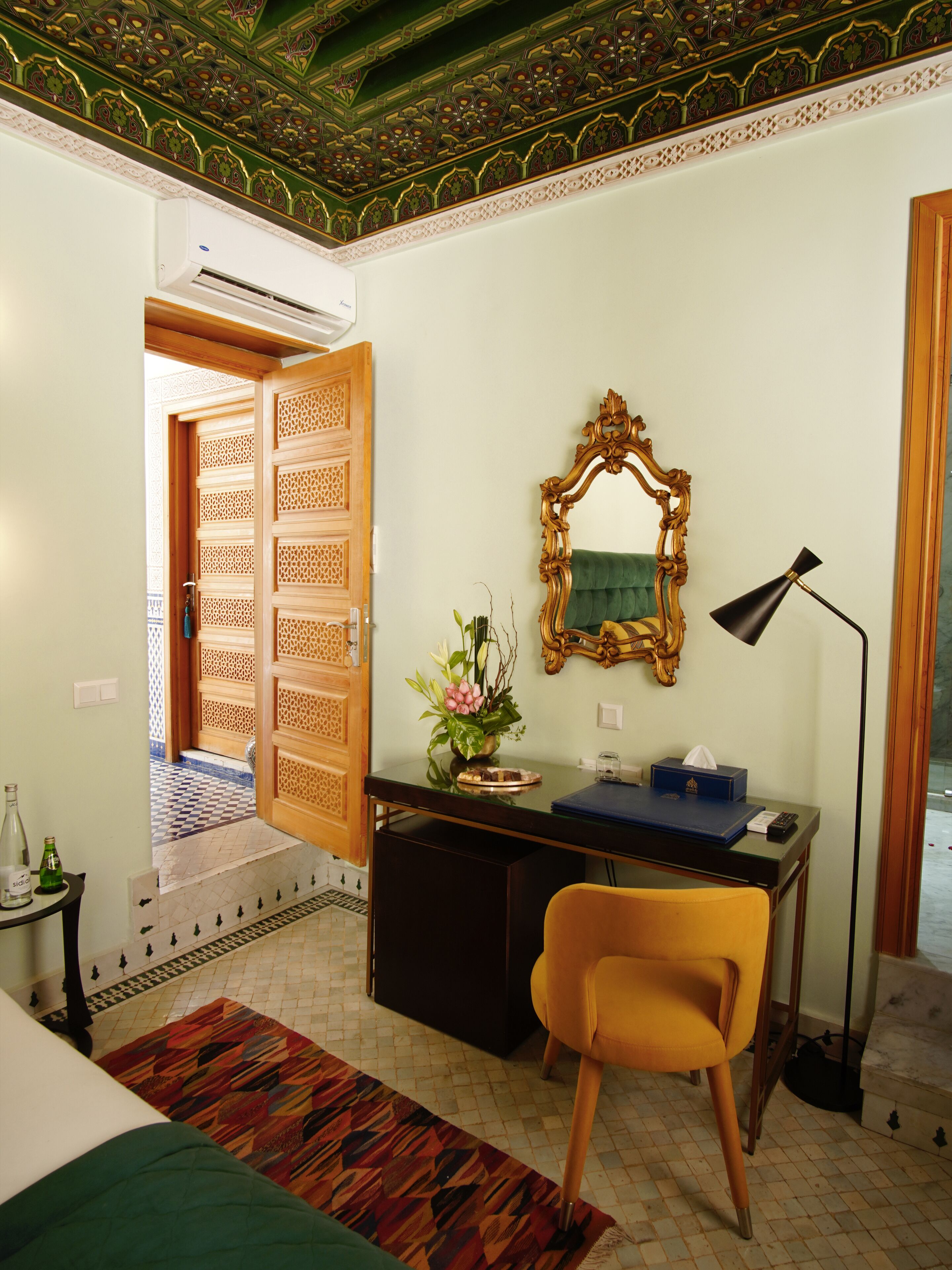 A room with a desk, chair, mirror, lamp, and decorative elements.