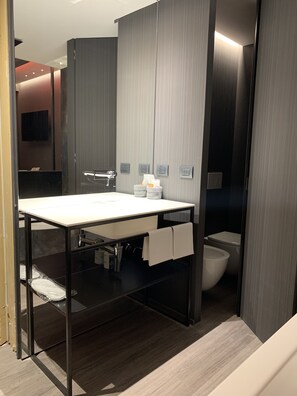 Un baño moderno con un lavabo blanco, tocador de madera oscura y un inodoro.