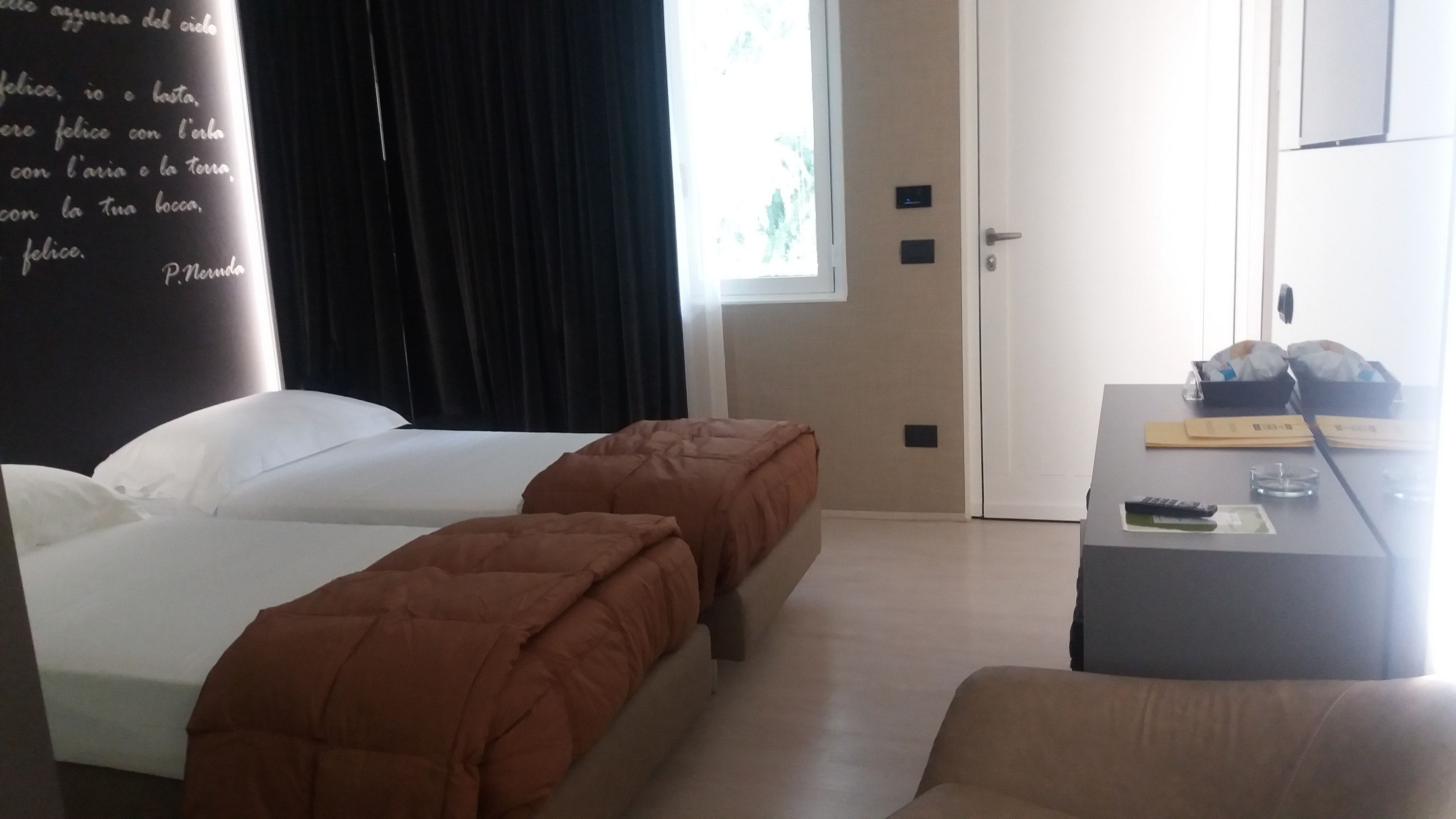 A hotel room with two beds, a desk, and a window.