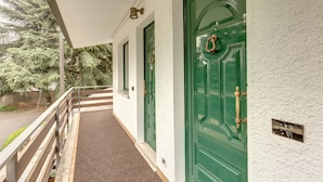 A covered porch with a wooden railing, a green door, and a mailbox on the wall.