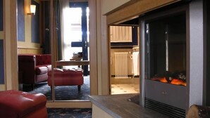 A modern living room with a fireplace, red leather sofa, and a dining area visible through a glass door.