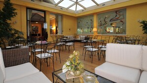 A spacious indoor area with multiple tables and chairs, a glass ceiling, and a large abstract art piece on the wall. - Hotel Terme Imperial (Montegrotto Terme)