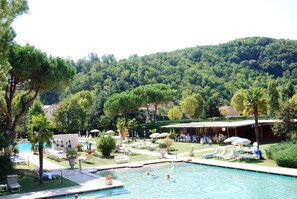 Un espace piscine agrémenté de chaises longues et de parasols, entouré de verdure et avec une colline en arrière-plan.