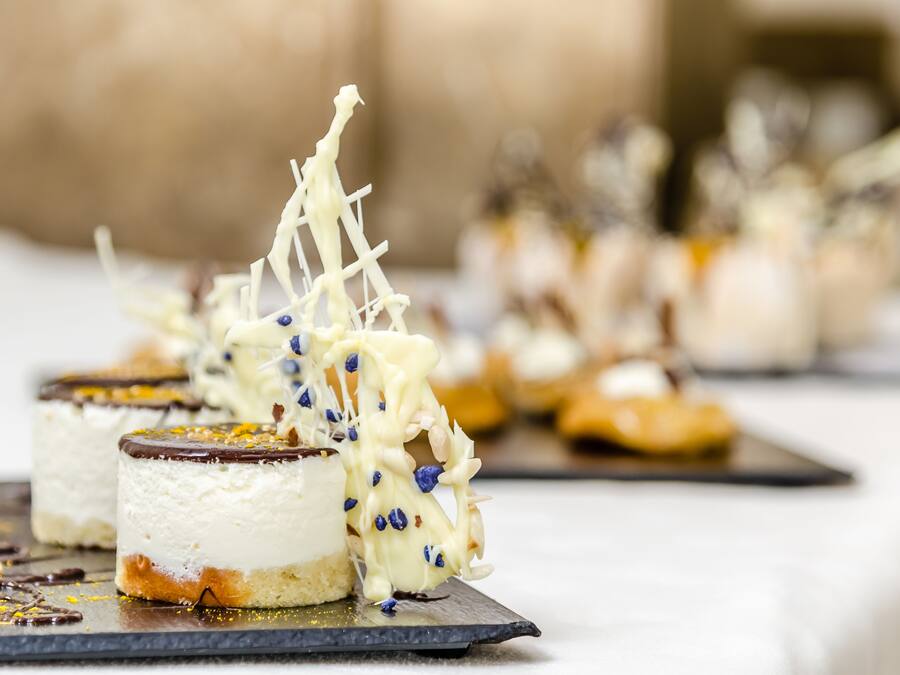 Eine Dessertauslage mit verschiedenen angerichteten Desserts, darunter ein Kuchen mit Schokoladenglasur und weißer Creme-Basis sowie ein Tarte mit goldbrauner Kruste.