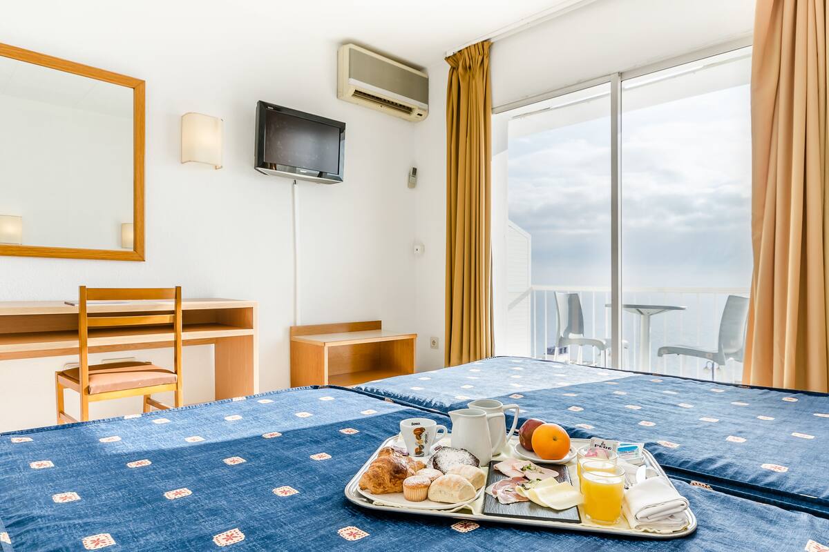 A hotel room with a bed, a desk, a chair, a TV, and a balcony with a view.