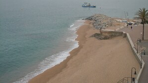A beach with a rocky shoreline, a boat in the distance, and a few people walking along the path. - Hotel Gran Sol (Sant Pol De Mar)
